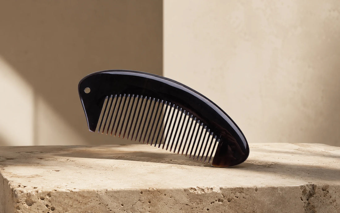 Black buffalo horn comb with fine teeth on stone, illustrating how to choose a horn comb for daily use