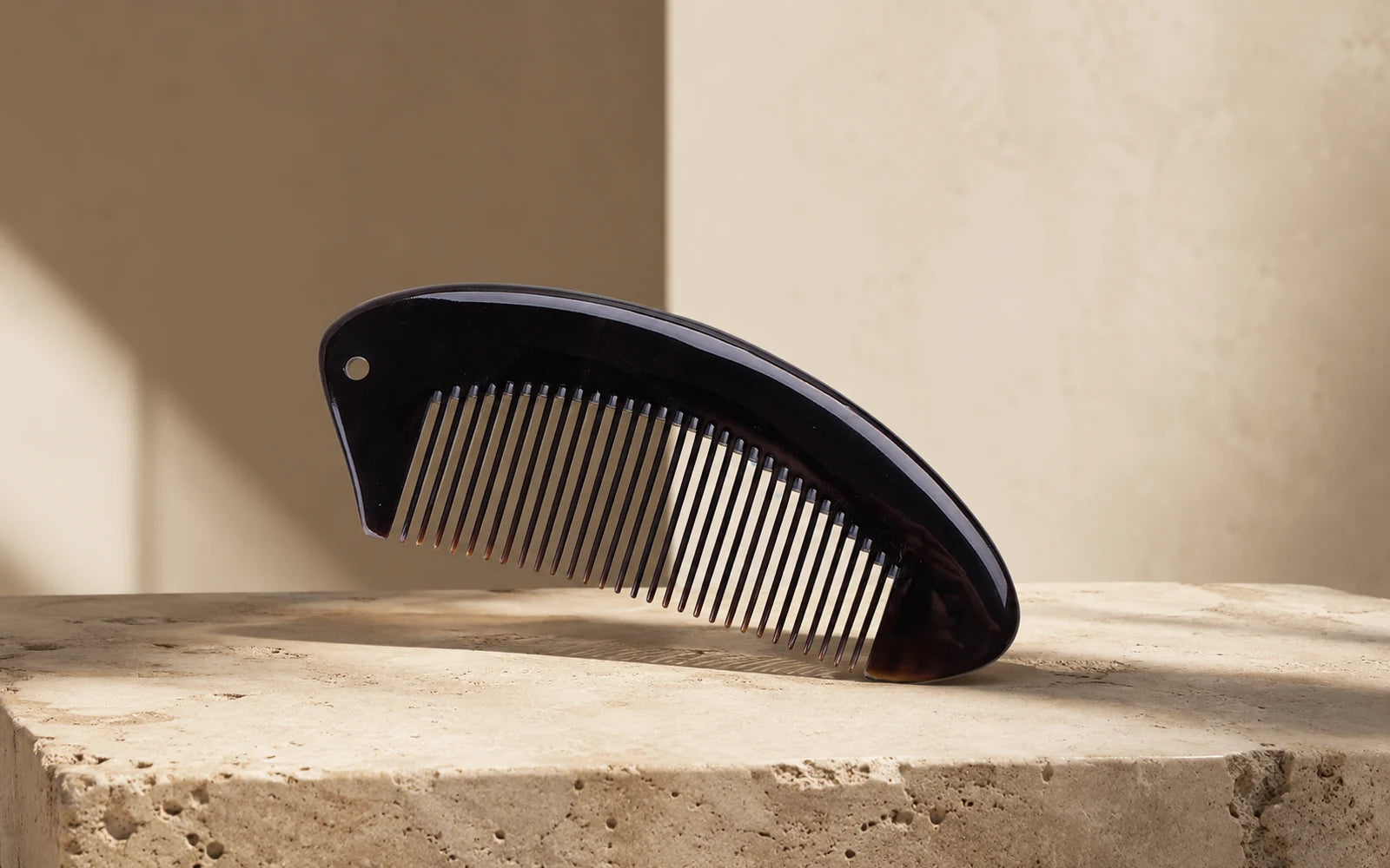 Black buffalo horn comb with fine teeth on stone, illustrating how to choose a horn comb for daily use