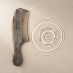 A Cozuy anti static comb resting by clear water ripples, perfect for a mindful scalp care routine to gently detangle.