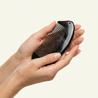 Hands holding a smooth black buffalo horn pocket comb, an ergonomic tool for targeted tension release.
