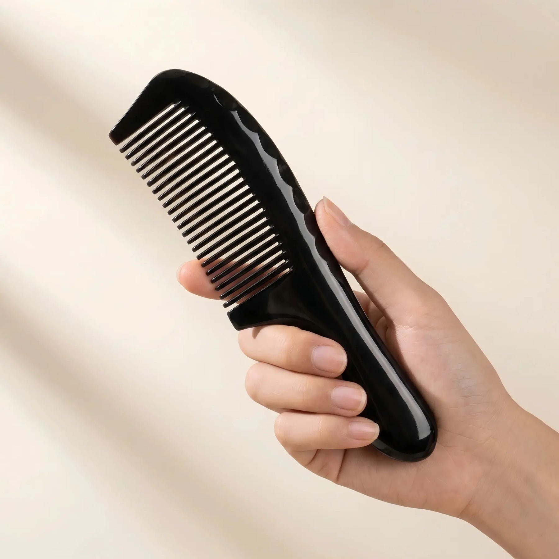 Hand holding COZUY black ox horn rounded-handle comb to show rounded handle and true hand scale. detail image 3