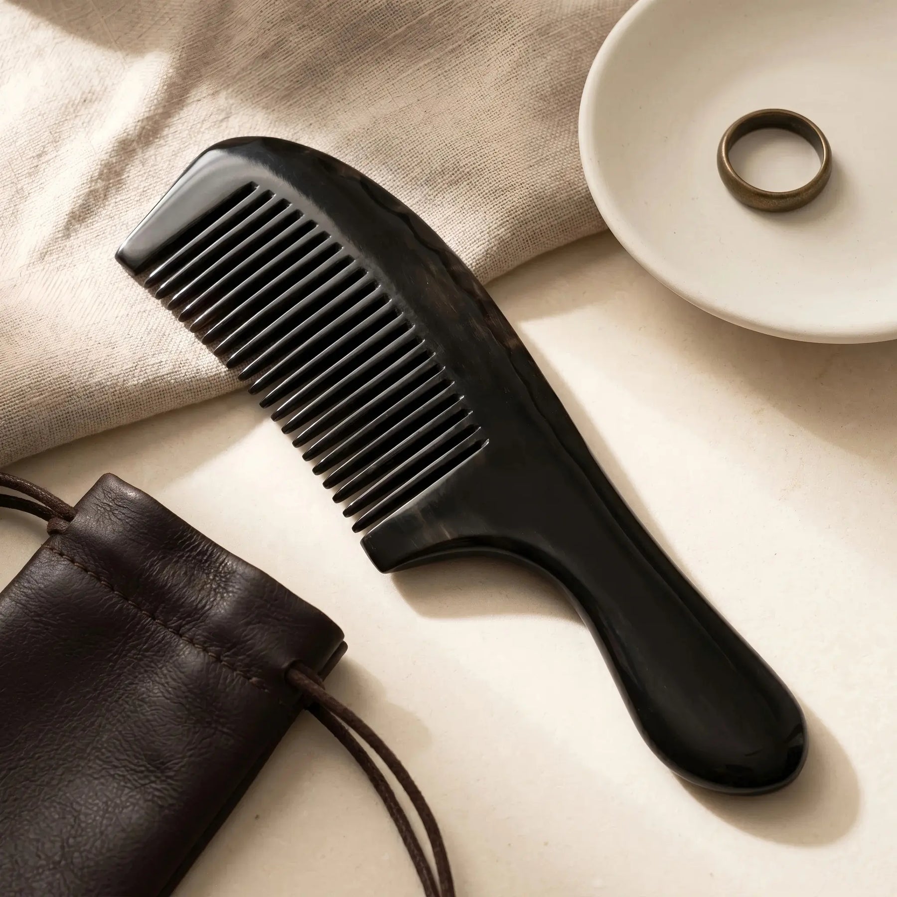 COZUY black ox horn rounded-handle comb in a styled still life showing deep black horn grain and polished surface. detail image 6