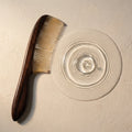 Ebony and translucent sheep horn comb beside water ripples on stone, an elegant tool for a calm scalp ritual.