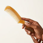 Hand gently holding a translucent yellow handled horn comb, designed for a daily tension relief ritual.