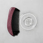 Natural horn comb beside water ripples on a light stone surface, suggesting a calm scalp ritual.