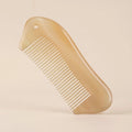 A translucent Cozuy natural horn comb standing on a beige background, designed to help reduce static.