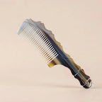 Sculpted yak horn comb with dark and light natural patterns resting on a beige background, an artisan gift.