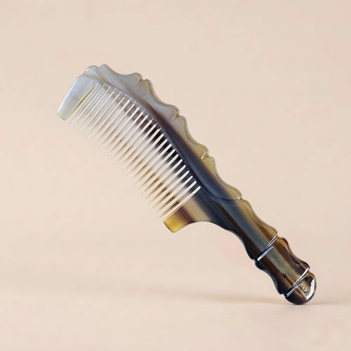 Sculpted yak horn comb with dark and light natural patterns resting on a beige background, an artisan gift.