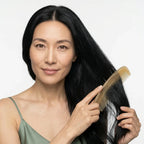 Smiling woman softly brushing her long black hair with a translucent sheep horn comb, premium anti-static hair care.
