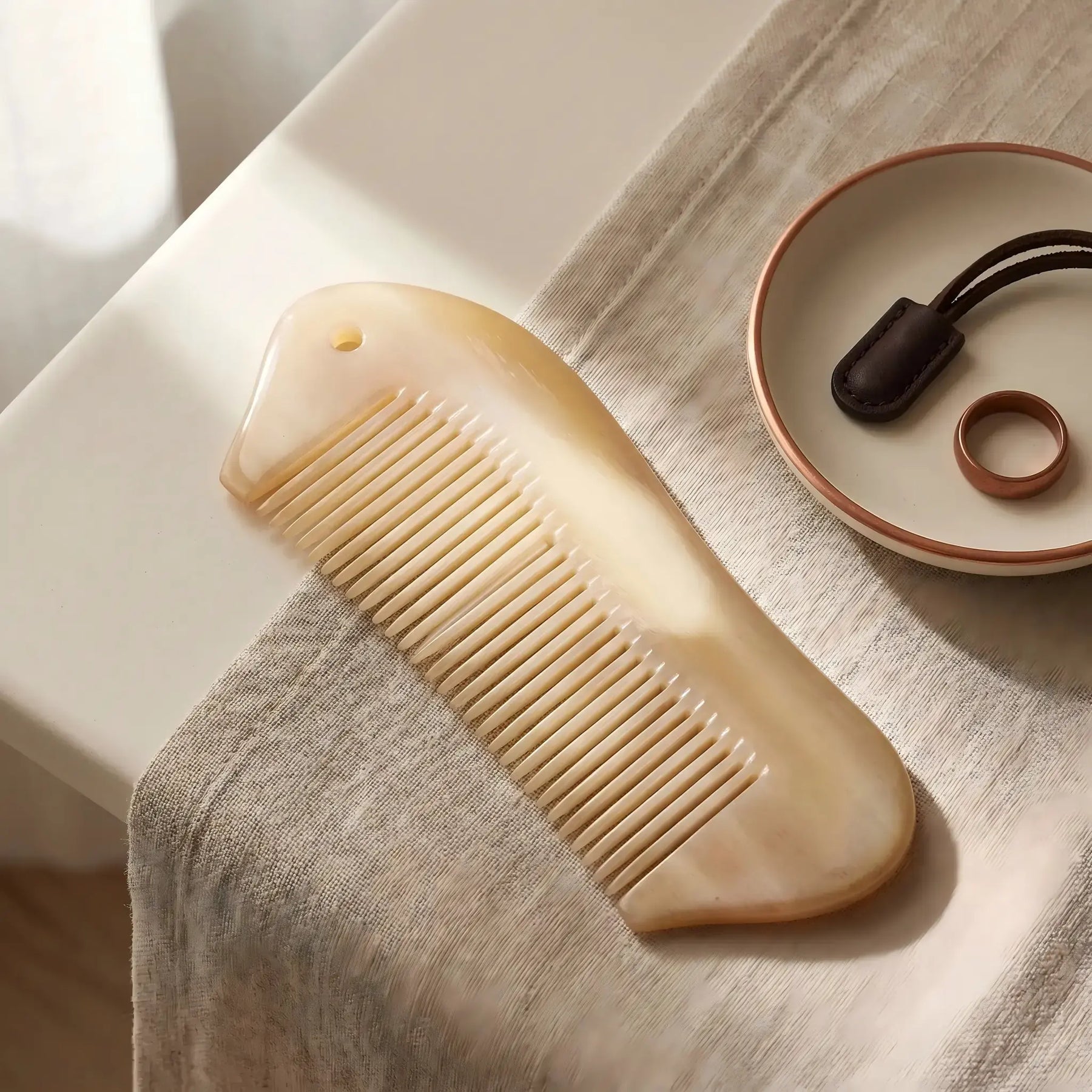 COZUY sheep horn pocket comb in a styled still life showing natural translucency and hanging-hole detail. detail image 6