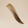 Long-handled natural horn comb with translucent brown patterns resting on a warm beige background