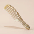Carved white yak horn comb with a twisted handle resting on a beige background, an elegant artisan gift.