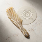 Carved white yak horn comb beside subtle water ripples on a light stone surface, suggesting a calm scalp ritual.