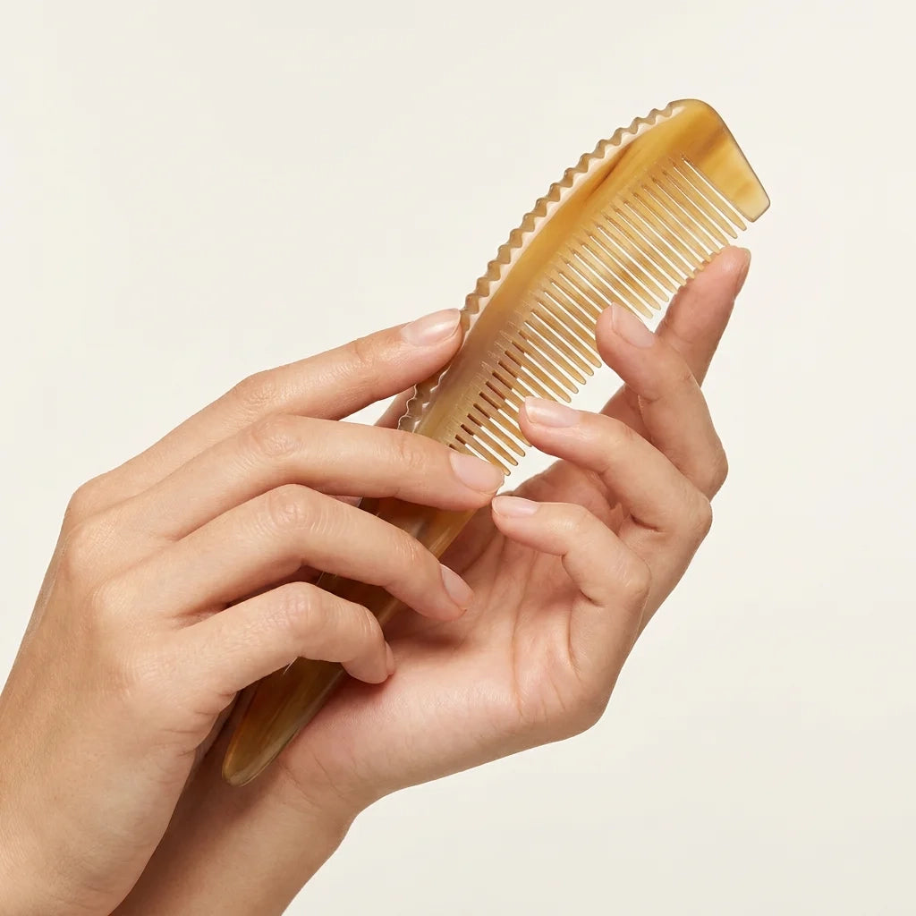 Hands gently holding a sculpted yellow buffalo horn comb with a pointed tip, an elegant artisan gift for hair wellness.