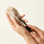 Hands holding a sculpted yellow buffalo horn comb with a pointed tip, an ergonomic tool for targeted tension relief.