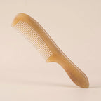 Elegant yellow natural horn comb with a handle resting on a soft beige background, a perfect artisan gift.