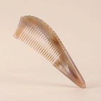 Pointed yellow natural horn gua sha comb resting on a beige background, an elegant tension and stress relief tool