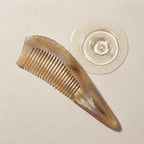 Pointed yellow horn comb resting beside subtle water ripples on a stone surface, suggesting a calm scalp ritual.