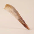 Pointed yellow buffalo horn gua sha comb floating on a beige background, an elegant tension and stress relief tool.