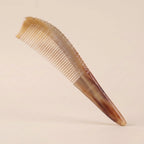 Pointed yellow buffalo horn gua sha comb floating on a beige background, an elegant tension and stress relief tool.