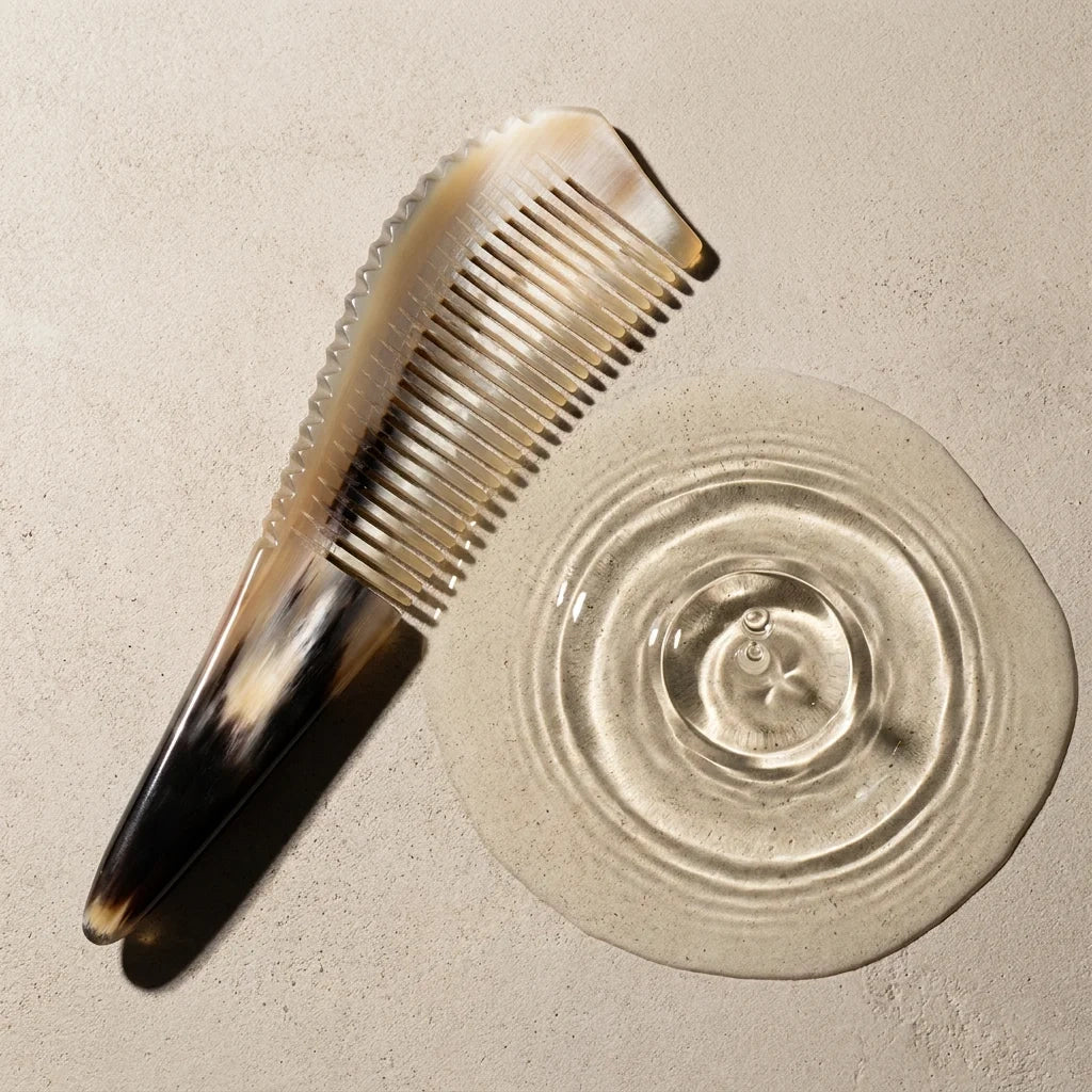 Sculpted yellow horn comb resting beside subtle water ripples on a stone surface, suggesting a calm scalp ritual.