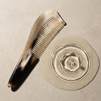 Sculpted yellow horn comb resting beside subtle water ripples on a stone surface, suggesting a calm scalp ritual.