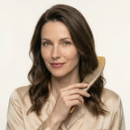 Serene woman holding a pointed yellow horn comb next to her wavy brown hair, featuraing premium anti-static hair care.